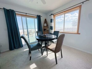 A room with a round table, two chairs, a ceiling fan, and a view of the sea through large windows. - Beach Club of Oscoda - All 4 Beachfront Cottages (Oscoda)