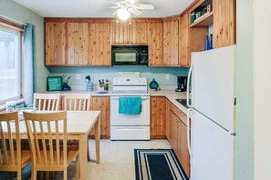 A kitchen with wooden cabinets, a white stove, a microwave, and a refrigerator. - Charming Lake Huron Cottage Private Beach Access (Oscoda)