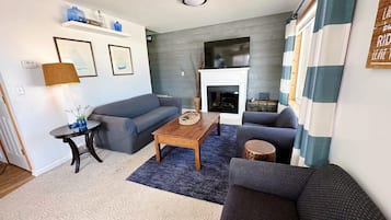 Una sala de estar con un sofá gris, una mesa de centro de madera, una chimenea y una cortina a rayas.