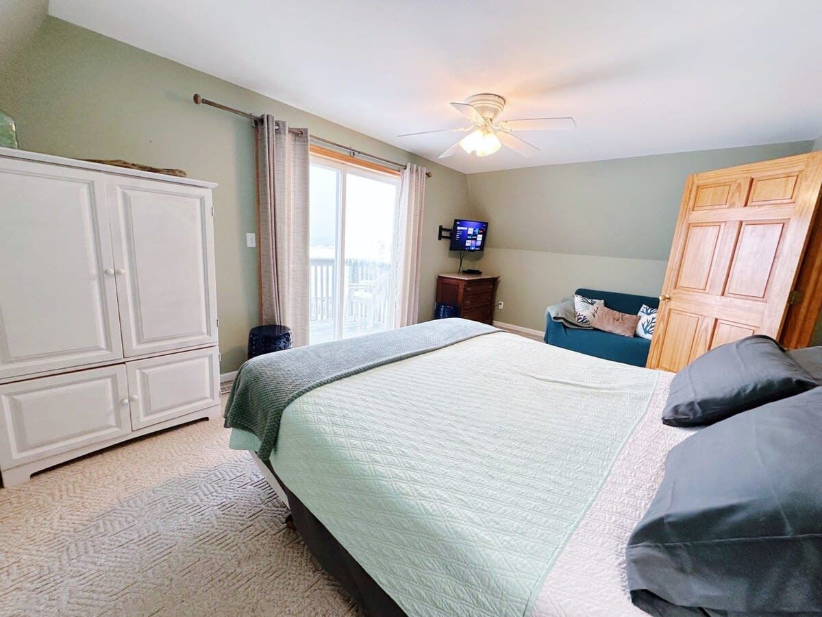 A bedroom with a bed, a wardrobe, a television, and a window with curtains.