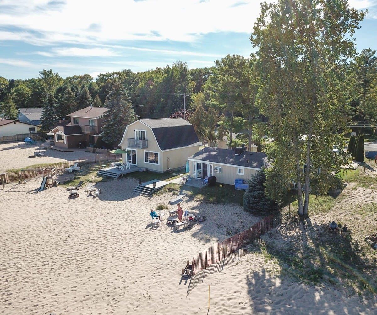 En ejendom ved stranden med et stort hus, en terrasse med udendørs møbler og et sandstrandområde.