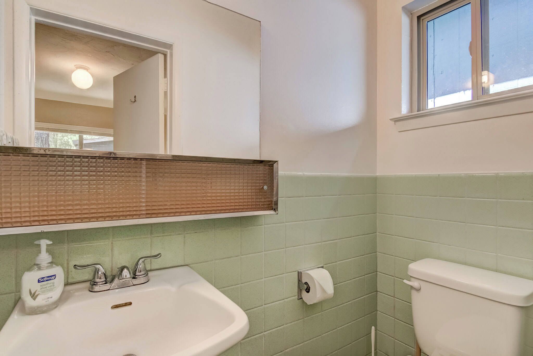A bathroom with a white sink, a mirror, a toilet, and a window.