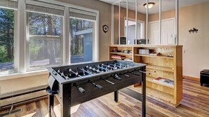 A room with a foosball table, large windows, a bookshelf, and a mirror.