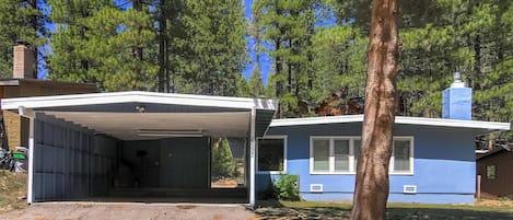 A single-story house with a covered garage, surrounded by tall pine trees.