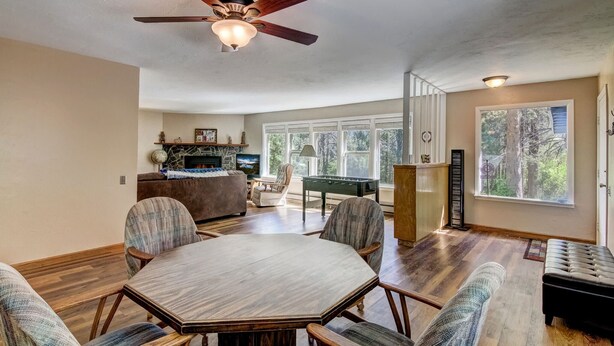 A spacious living room with a round table, comfortable seating, a fireplace, and large windows offering a view of the outdoors.