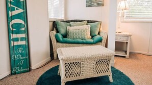 A cozy room with a wicker sofa and ottoman, a teal rug, and a 'BEACH' sign. - Stunning views of Lake Huron (Oscoda)
