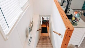 A staircase with a wooden handrail, a white wall, and a door leading to a room with a table and chairs. - Stunning views of Lake Huron (Oscoda)