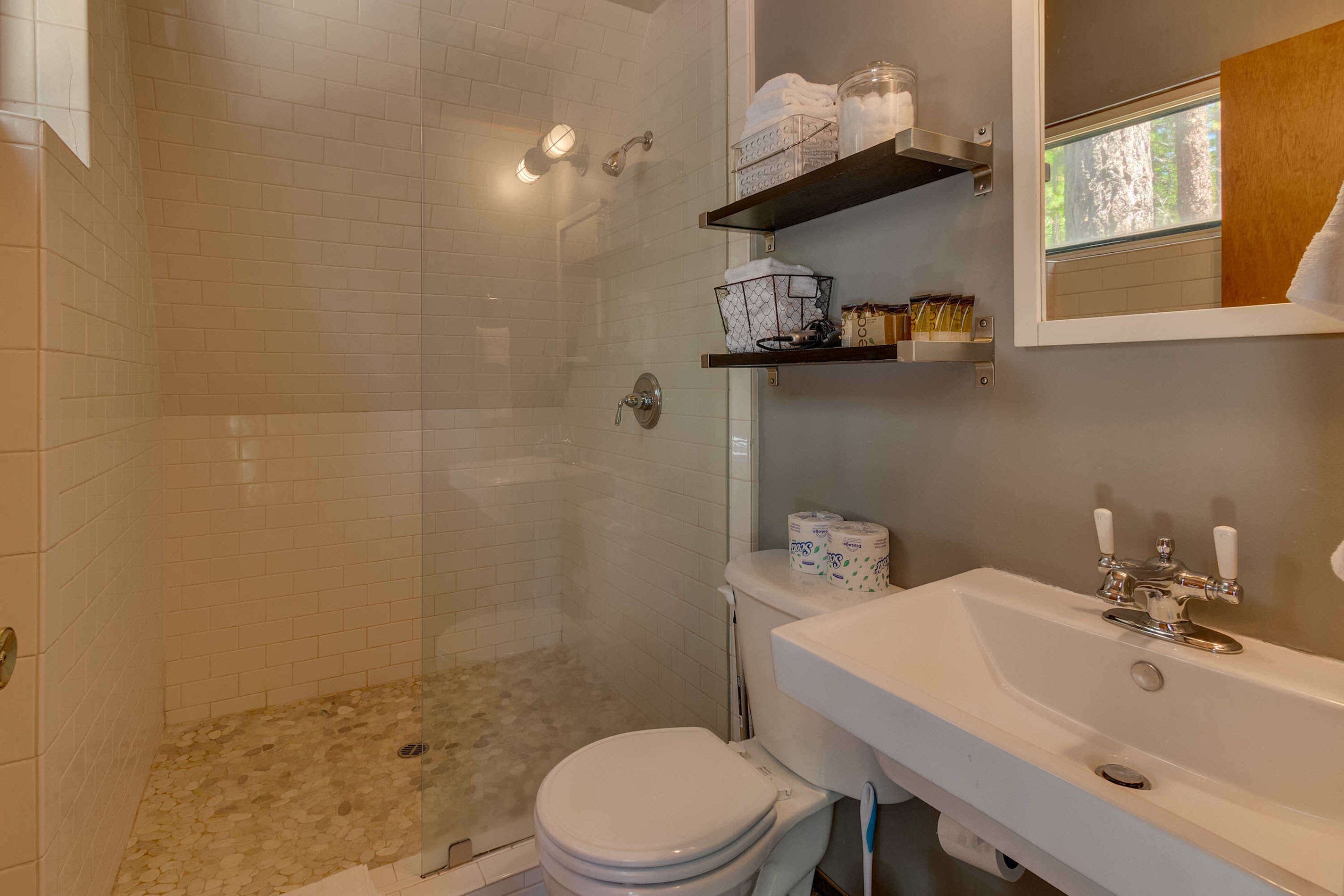 A bathroom with a shower, toilet, sink, and shelves with toiletries.