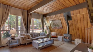 A cozy living room with a wooden ceiling, a sofa, a glass coffee table, a lamp, a fireplace, and a framed picture of a bear.