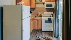 A compact kitchen with wooden cabinets, a white refrigerator, a microwave, and a stove.