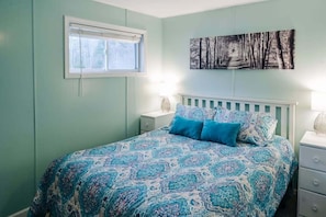 A bedroom with a bed, a nightstand, a window, and a wall-mounted picture.