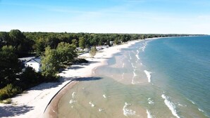 A coastal beach with a sandy shoreline, a clear sky, and a forested area in the background.