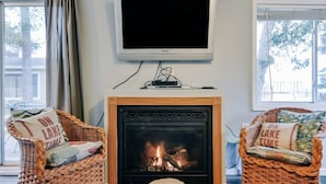 A living room with a fireplace, two wicker chairs, a television, and a window.