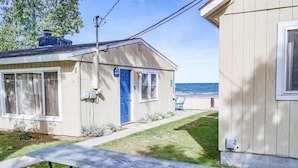 A small, single-story building with a blue door and windows, a picnic table in the foreground, and a view of the ocean in the background. - Beachfront cottage on Lake Huron (Oscoda)