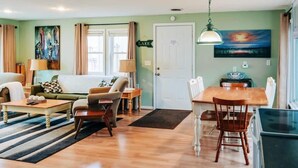 A living room with a sofa, armchairs, a coffee table, and a dining table with chairs. There is a painting on the wall, a lamp, and a door labeled "LAKE". - Beachfront cottage on Lake Huron (Oscoda)
