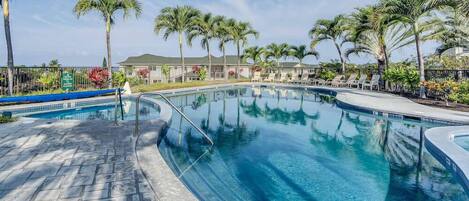 A swimming pool with clear blue water, surrounded by palm trees and lounge chairs.