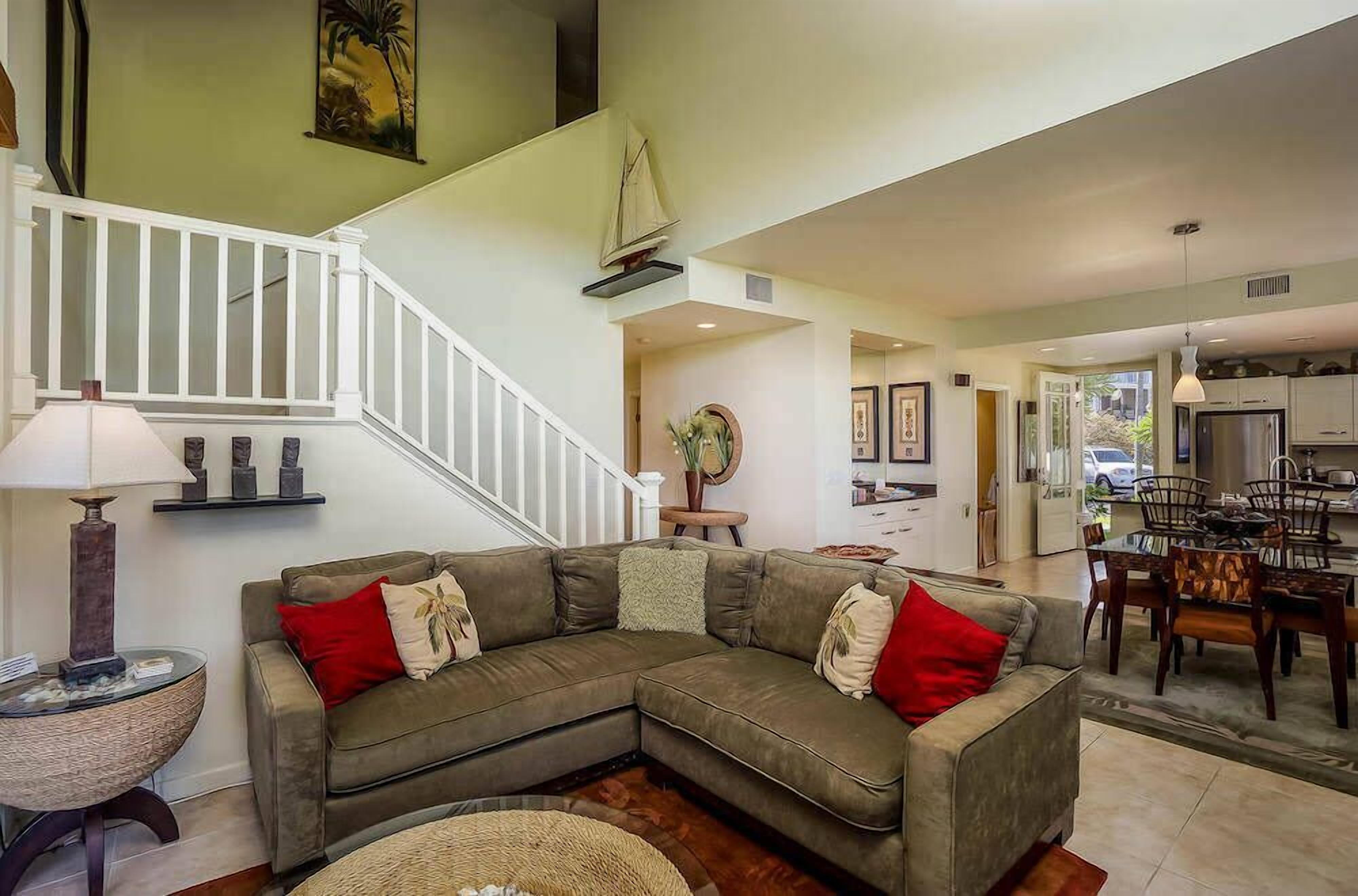 A spacious living room with a sectional sofa, a dining area with wooden chairs, a staircase, and a kitchen visible through an open door.