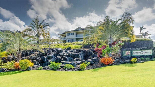 A hotel with a sign reading "Na Hale Keauhou," featuring a landscaped garden with palm trees, a waterfall, and a well-maintained lawn. - Luxury at Na Hale O Keauhou #N1 (Kailua-Kona)