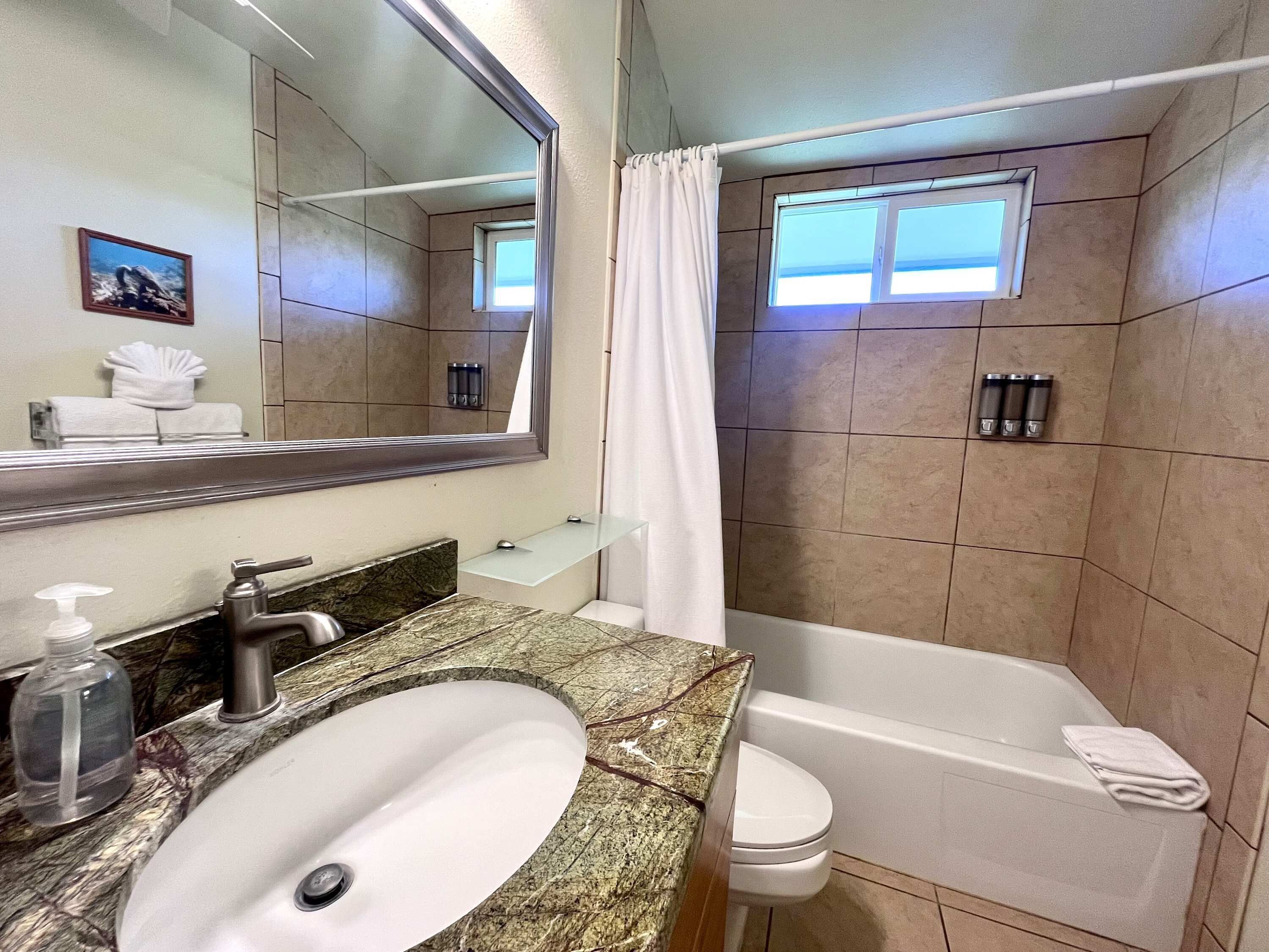 Ein Badezimmer mit Marmorwaschbecken, Badewanne, Duschvorhang und Fenster.
