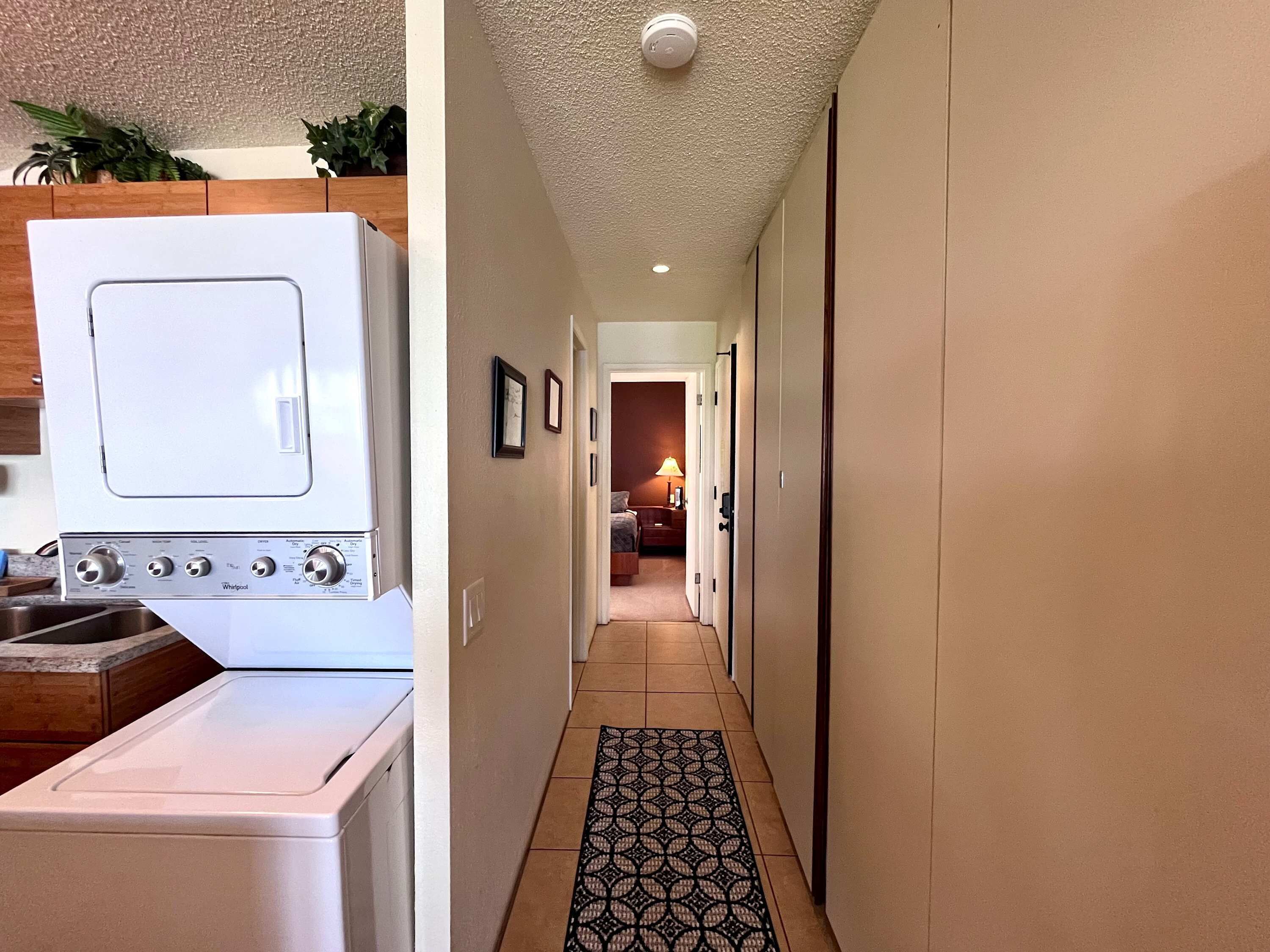 A laundry area with a white washer and dryer, a hallway with a patterned rug, and a door leading to a bedroom.