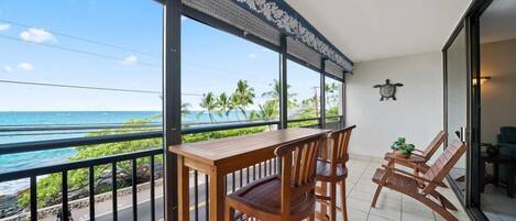 A balcony with a wooden table and chairs, a view of the ocean, and a decorative ceiling.