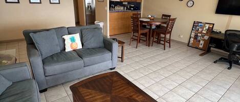 A living room with a gray sofa, a wooden coffee table, and a dining area with wooden chairs and a table.