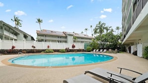 Ein Swimmingpool mit Liegestühlen, Palmen und einem Gebäude mit Balkonen.