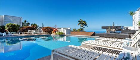 A poolside area with lounge chairs and a view of the ocean.