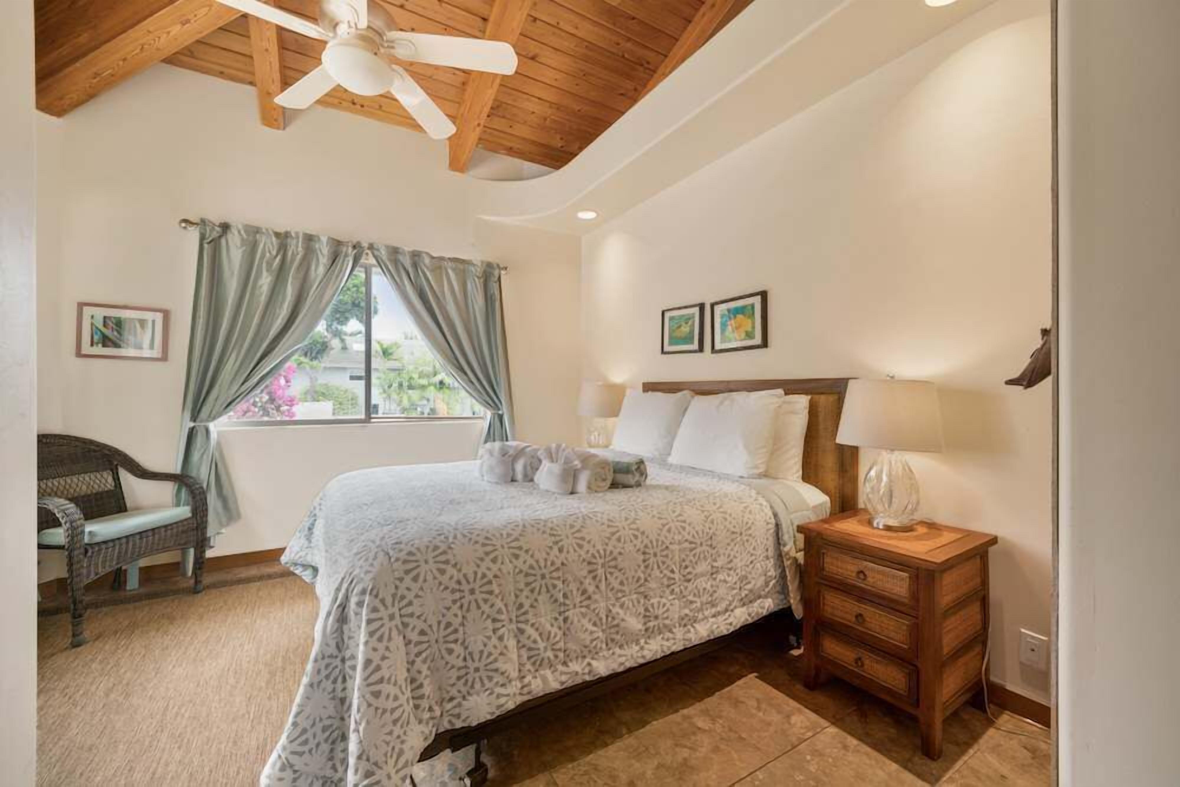 A bedroom with a bed, a nightstand, a chair, a window with curtains, and a ceiling fan.