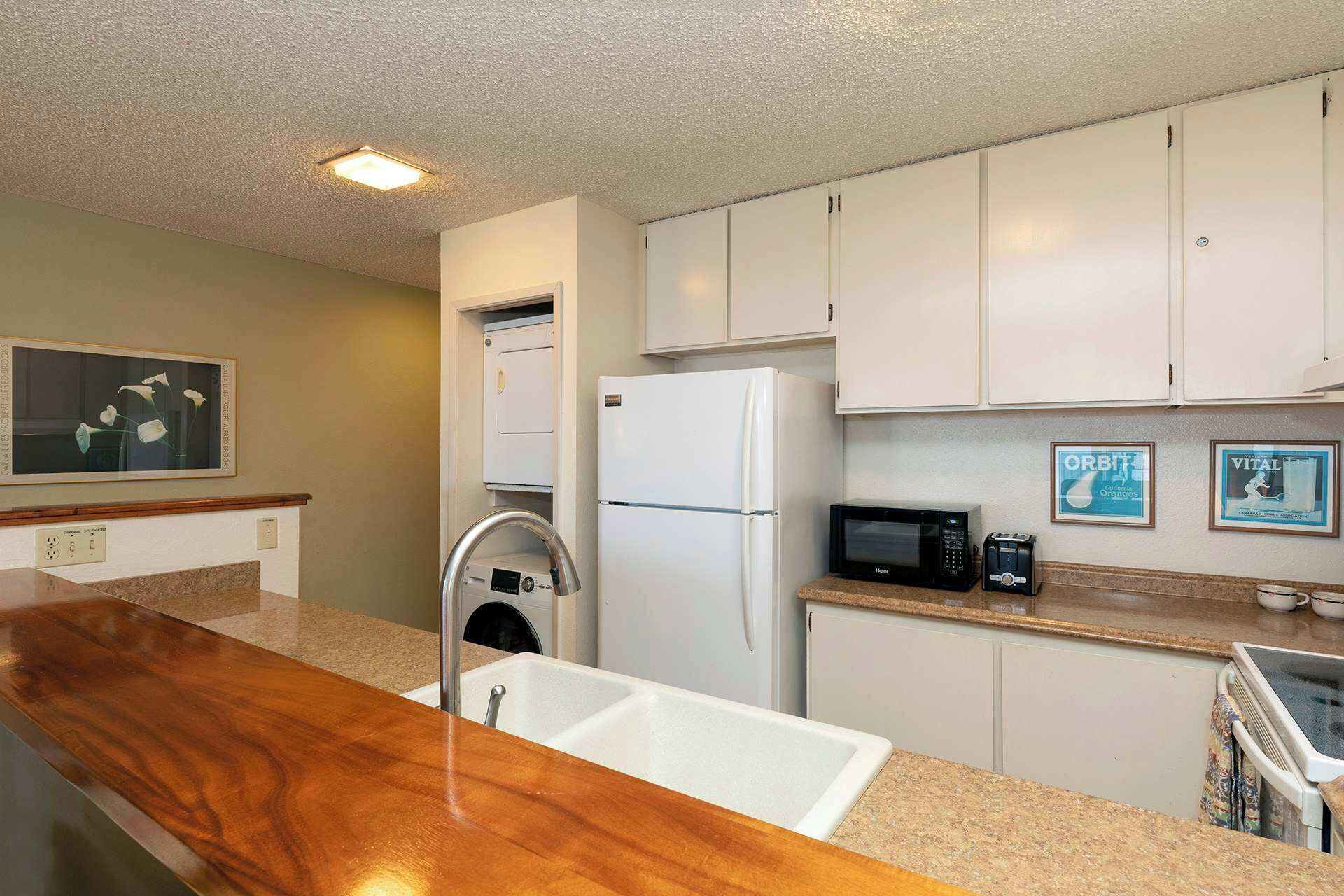 A compact kitchen with white cabinets, a built-in microwave, a refrigerator, and a wooden countertop.