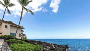 A beachfront property with a two-story building, a stone retaining wall, and a view of the ocean.