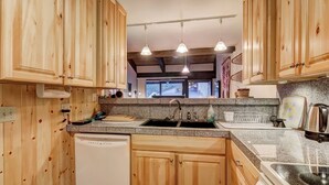A kitchen with wooden cabinets, granite countertops, a dishwasher, a sink, and pendant lighting.
