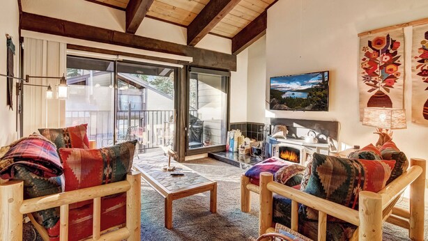 A cozy living room with wooden furniture, a fireplace, and a large TV on the wall.