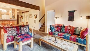 A cozy living room with a wooden sofa and armchair, a coffee table, and a staircase leading to another room.