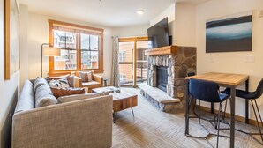A cozy living room with a sofa, coffee table, and a fireplace. There is a dining area with a table and chairs.