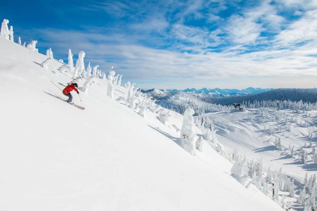 Eine verschneite Berglandschaft mit einem Skifahrer in einer roten Jacke.