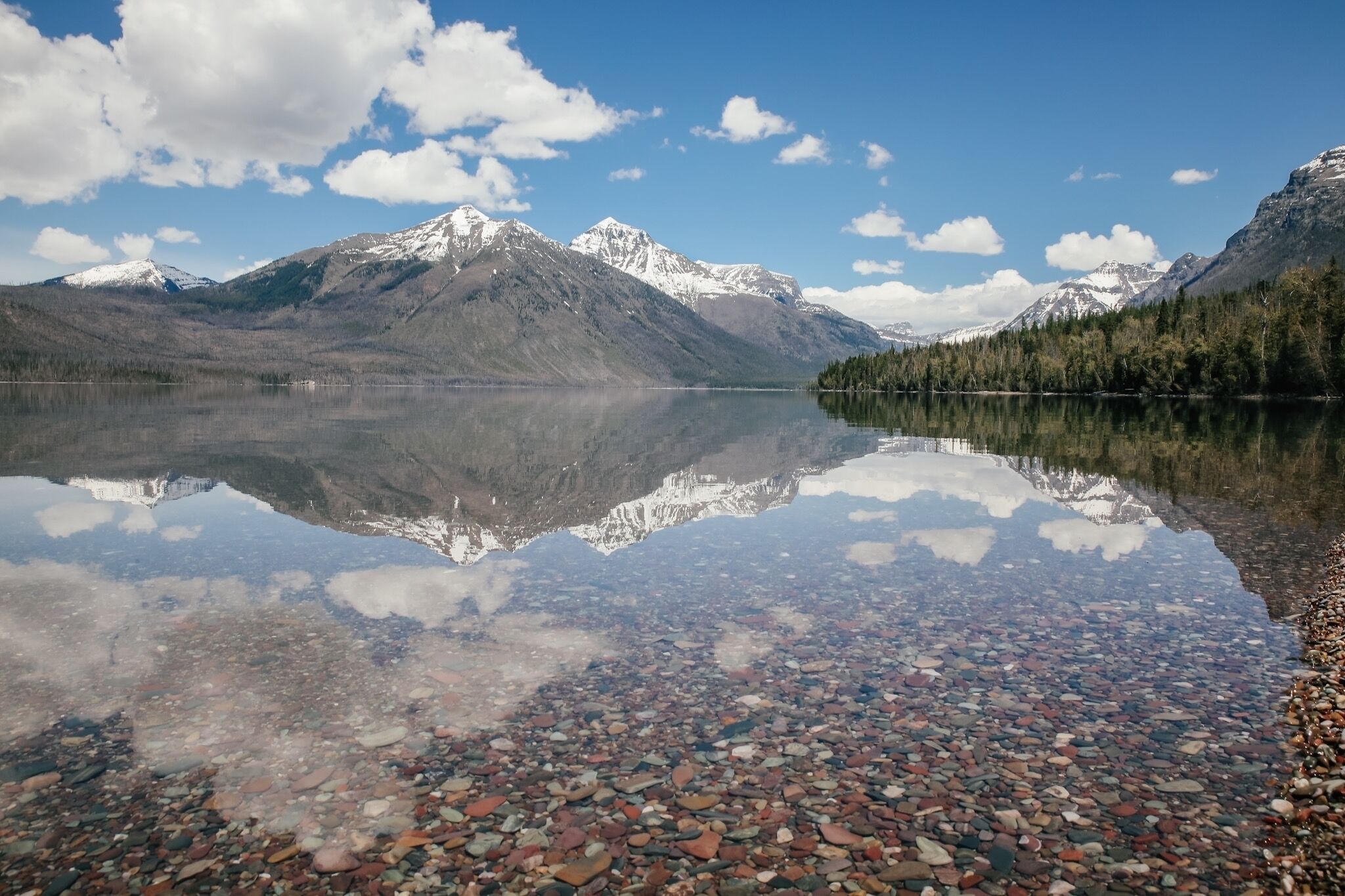 A clear lake reflecting mountains and a forested area.