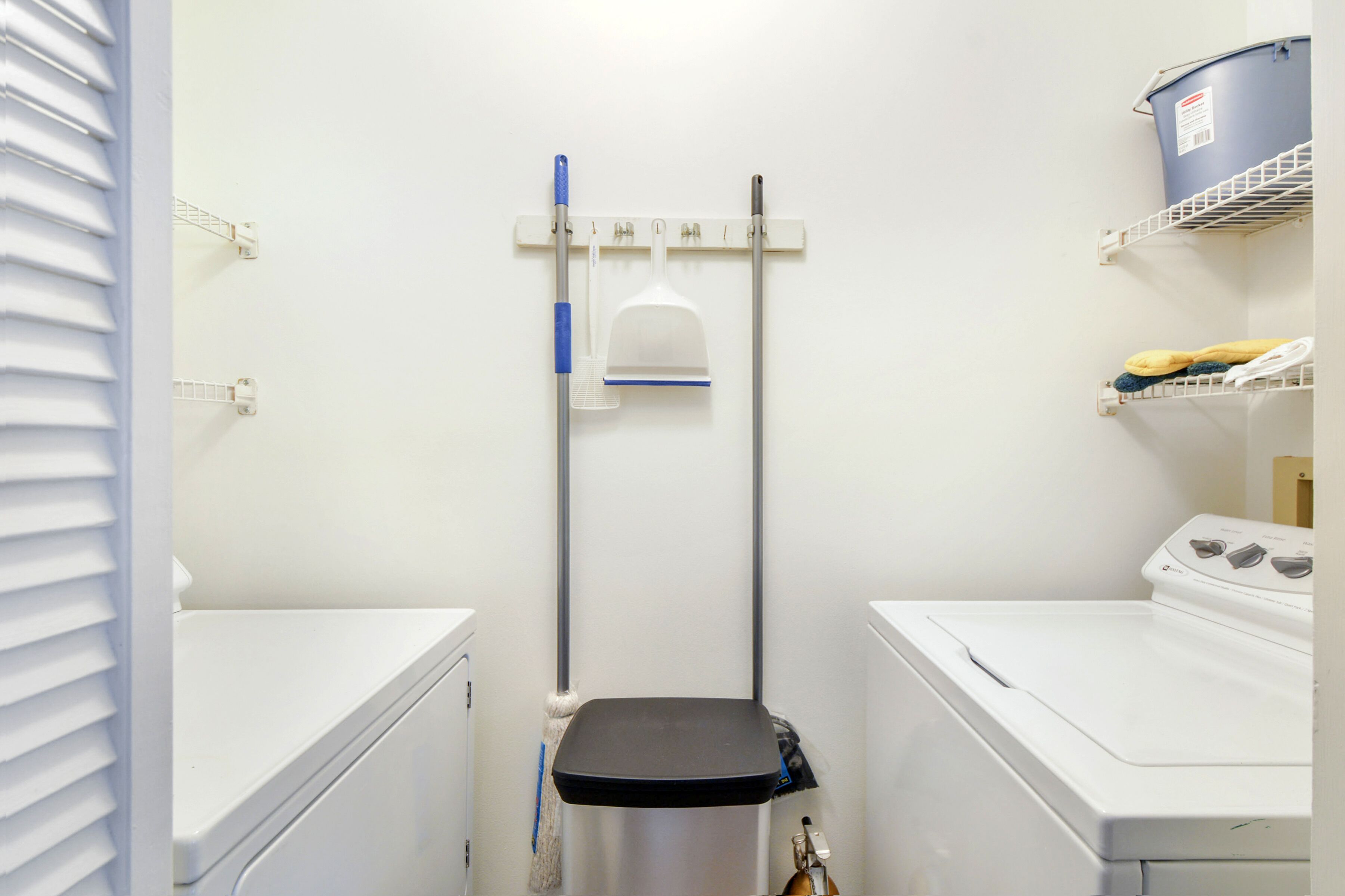 A laundry room with a washing machine, dryer, and a mop rack on the wall.
