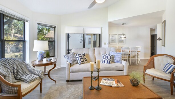 A spacious living room with a sofa, armchairs, a coffee table, and a dining area in the background.