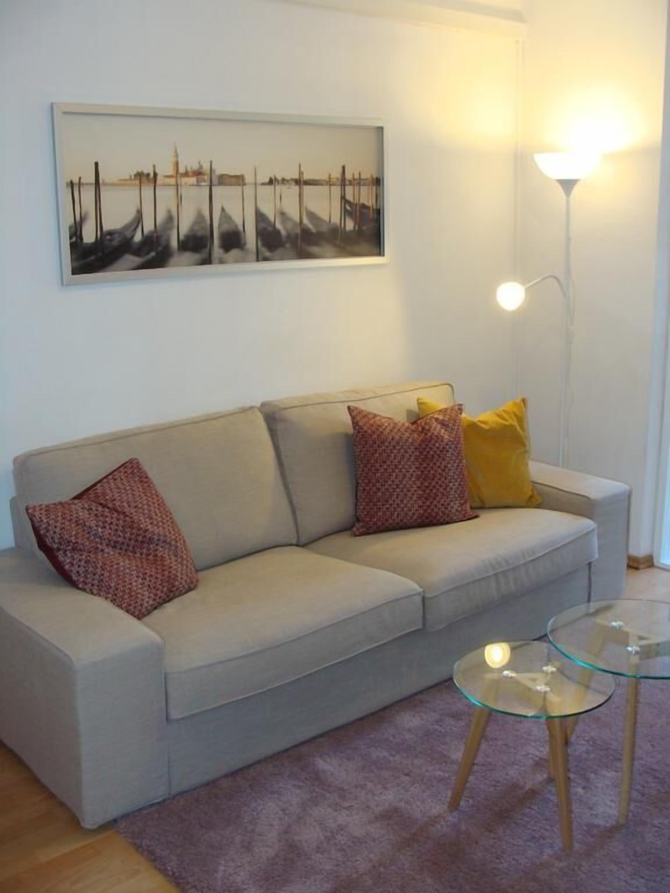 Un soggiorno con un divano, due tavolini in vetro, una lampada e un quadro appeso al muro.
