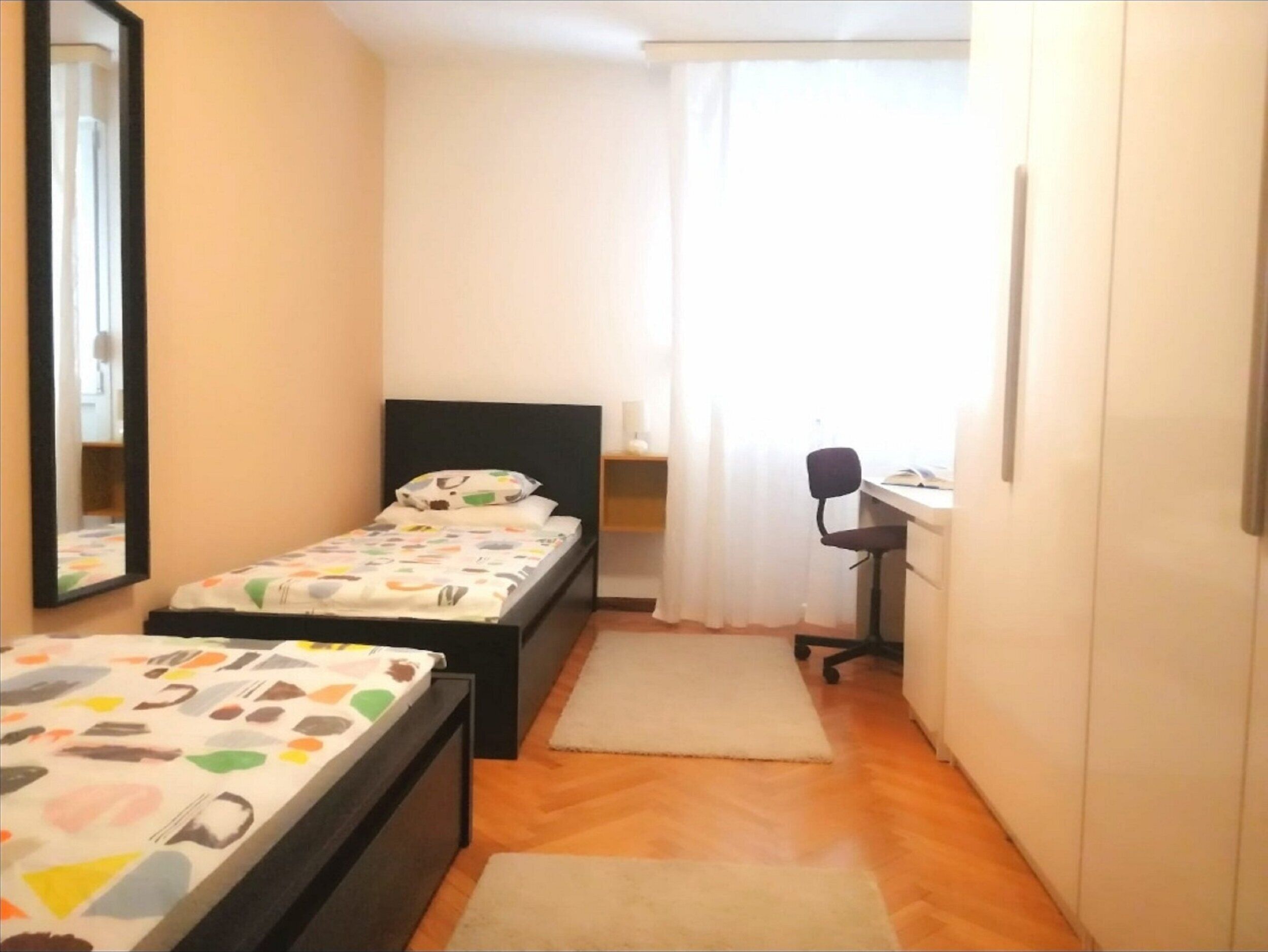 Une petite chambre à coucher, de taille réduite, comprenant un lit simple, un bureau et une chaise.