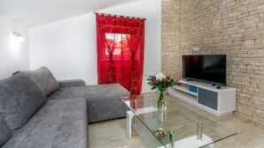 Una sala de estar moderna con un sofá gris, una mesa de centro de vidrio, un televisor de pantalla plana sobre un mueble blanco y una pared con diseño de ladrillo.