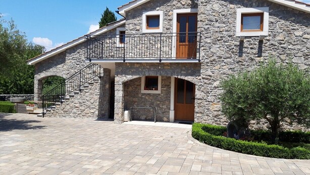 Una casa de piedra con balcón, una escalera y un camino de entrada pavimentado.