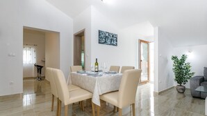 Un comedor con una mesa redonda dispuesta para seis personas, sillas color beige, una planta en maceta y un cuadro en la pared.