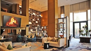 A spacious lobby with a large flat-screen TV displaying a fireplace, multiple seating areas, a large bookshelf, and a large window providing natural light. - Braira Al Yarmouk Hotel (Riyadh)
