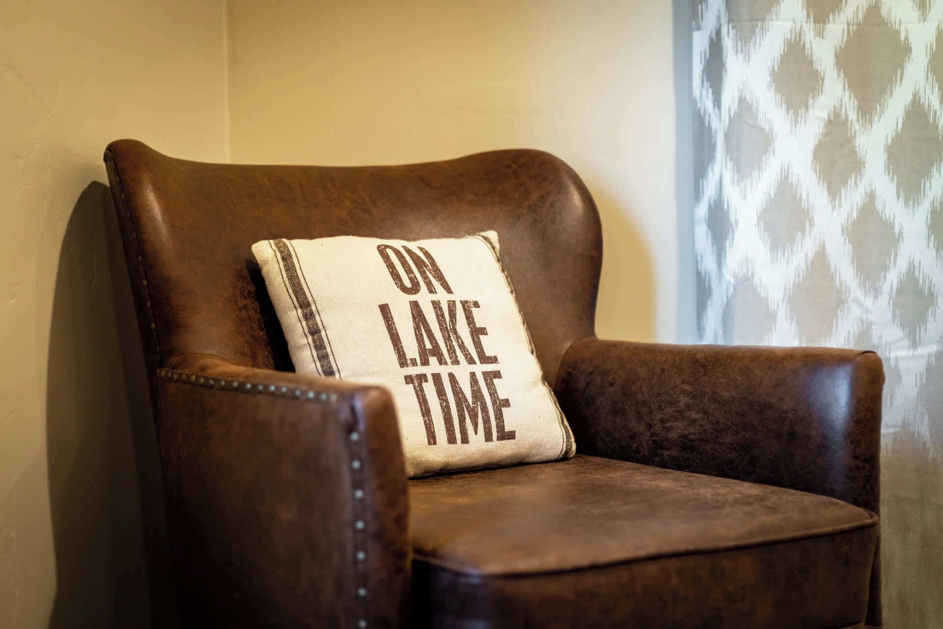 A brown leather armchair with a cushion that reads "ON LAKE TIME."