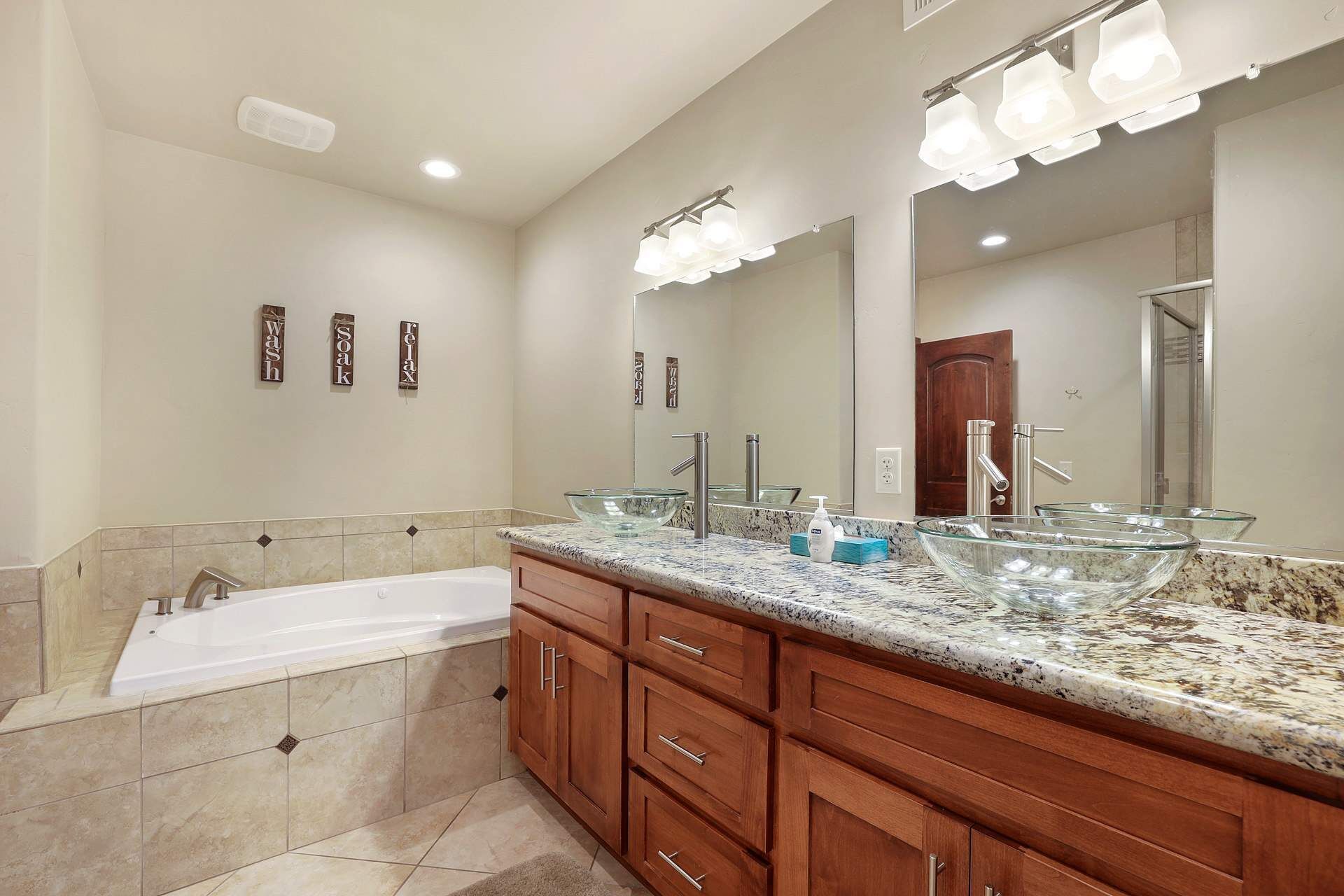 A modern bathroom with a large glass sink, a bathtub, and a vanity with drawers.
