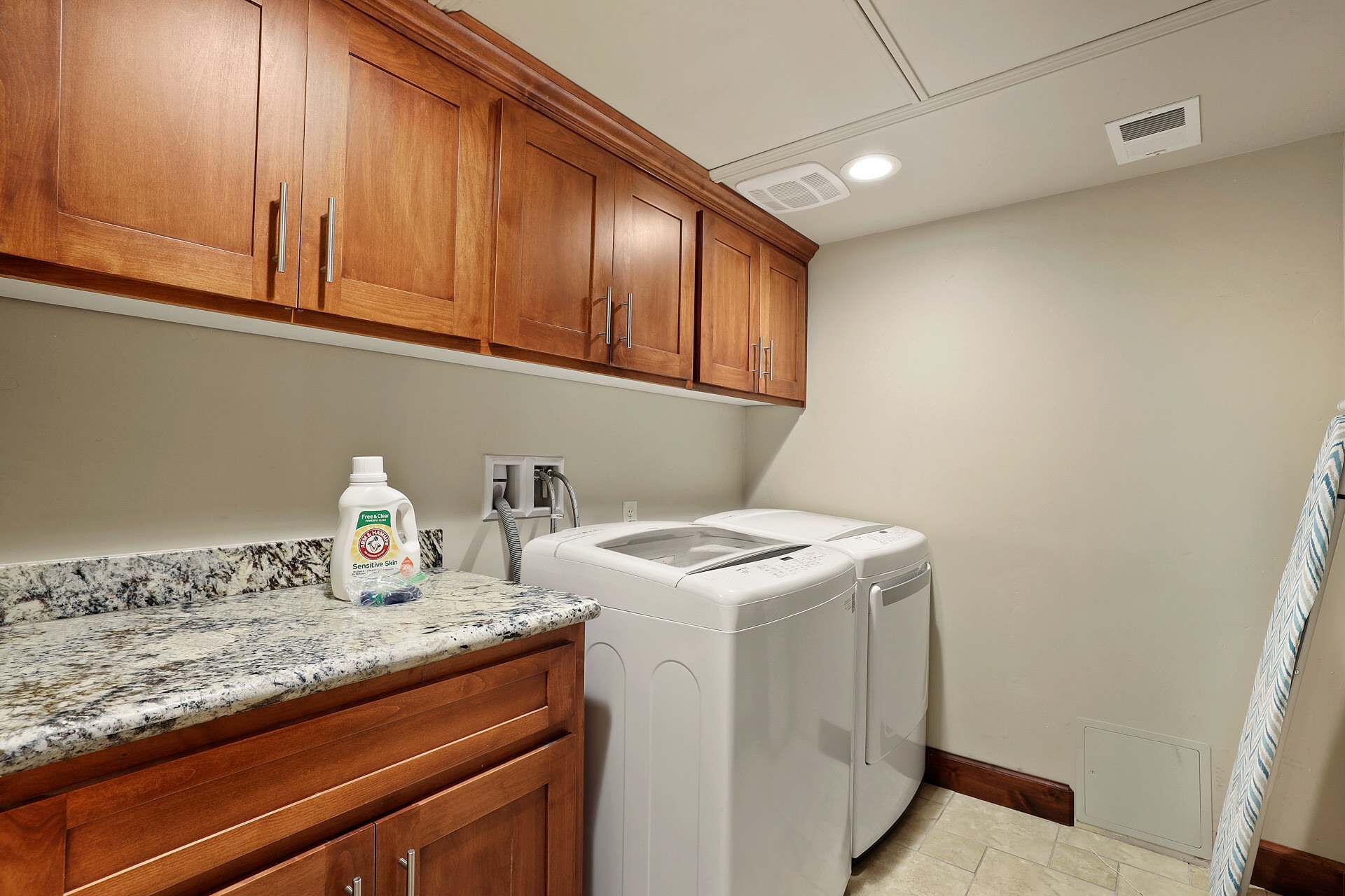 A laundry room with a washing machine, a dryer, wooden cabinets, and a granite countertop.