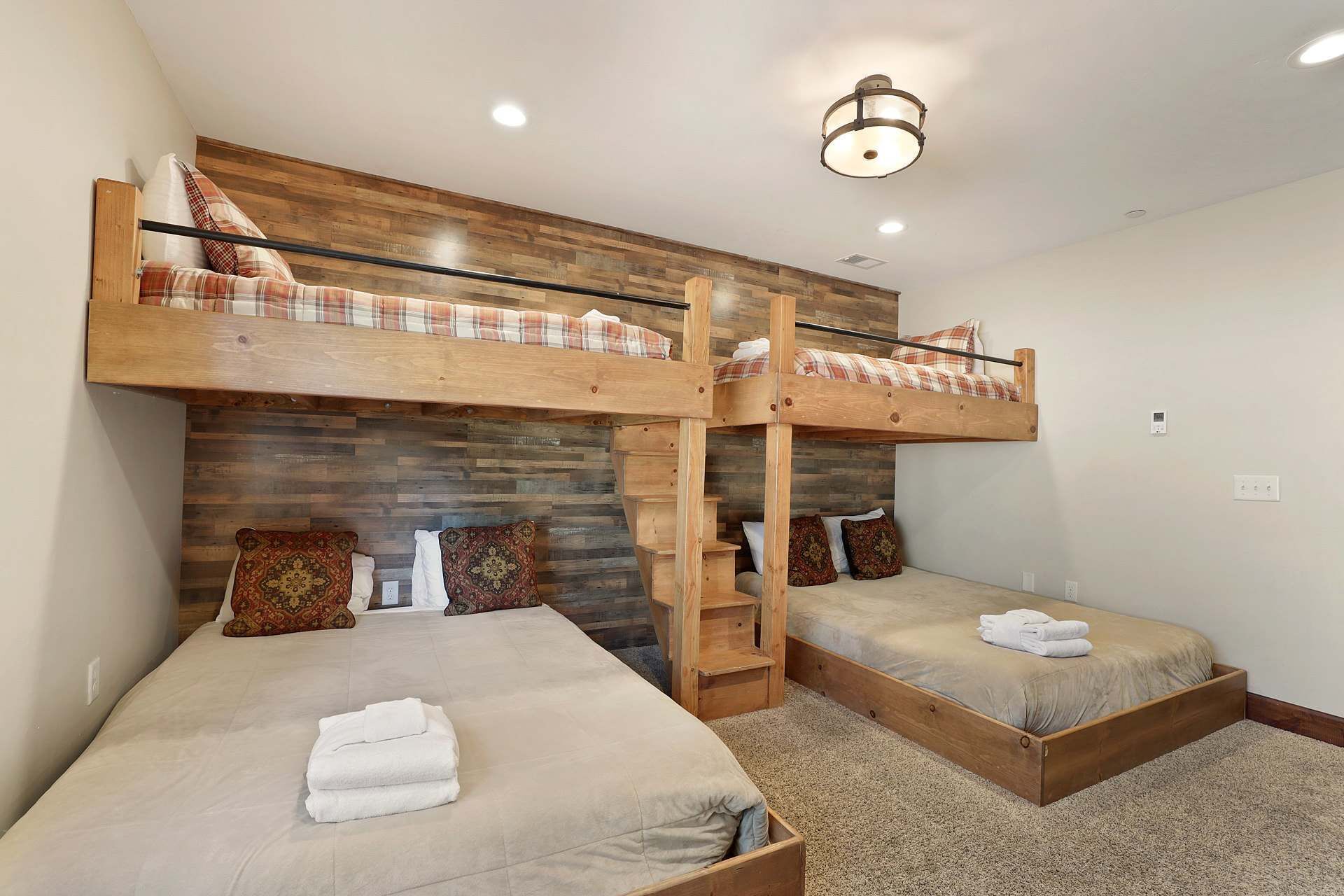 Una habitación con dos literas, cada una con estructura de madera y colchón. Tiene un cabecero de madera con un diseño estampado, y una pequeña escalera de madera adosada a los lados de las camas.