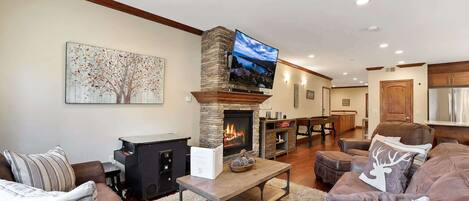 A living room with a stone fireplace, a television mounted above it, and a large painting on the wall.